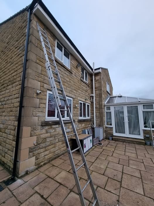 An extension ladder set up against the side of a two-story home, prepared for accessing and clearing roof gutters.