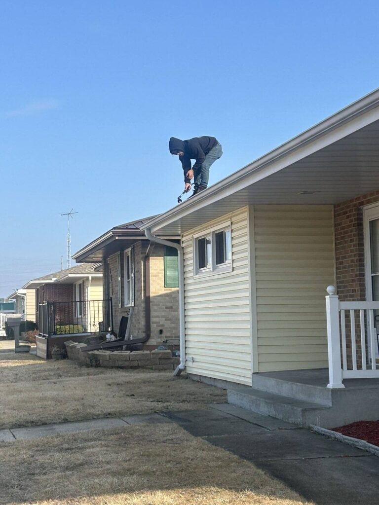 Professional gutter cleaning technician removing debris from a residential roof in Rochester, NY as part of our step-by-step gutter maintenance process.